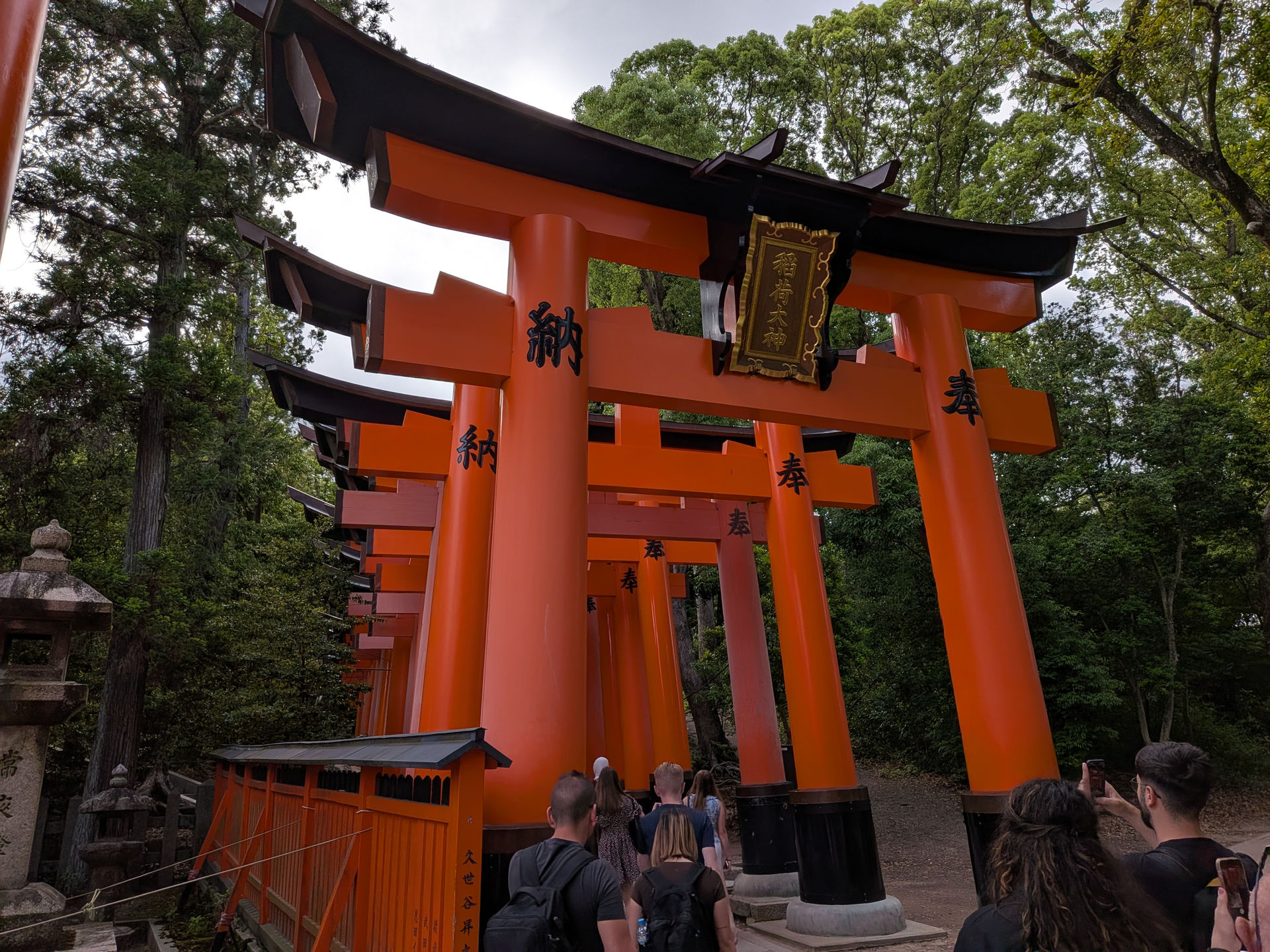 A photograph of a red Torii gate at Fushimi Inari Shrine, tourists are taking photos.